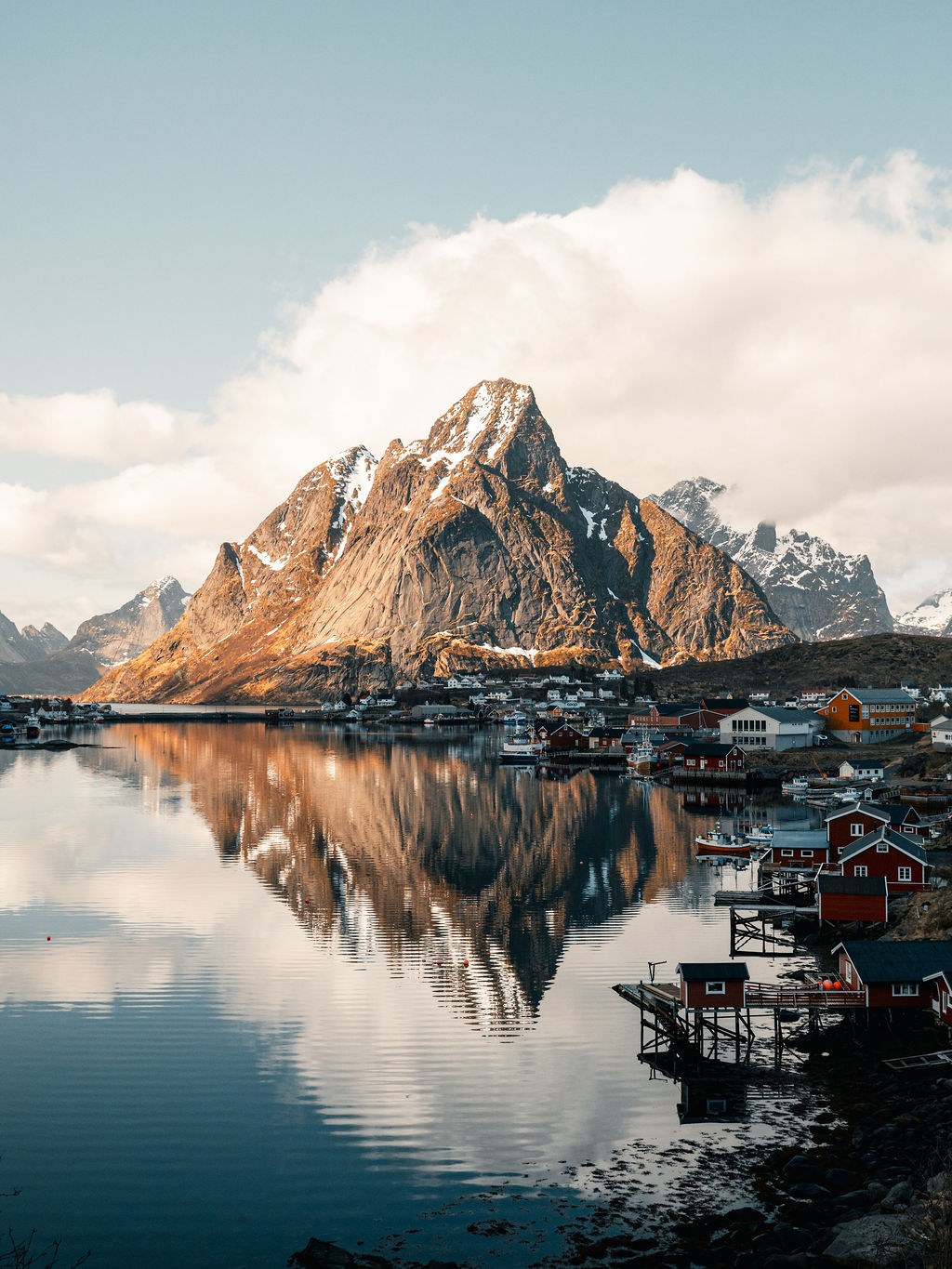 Fjell og rorbuer speiler seg i vannet i Lofoten